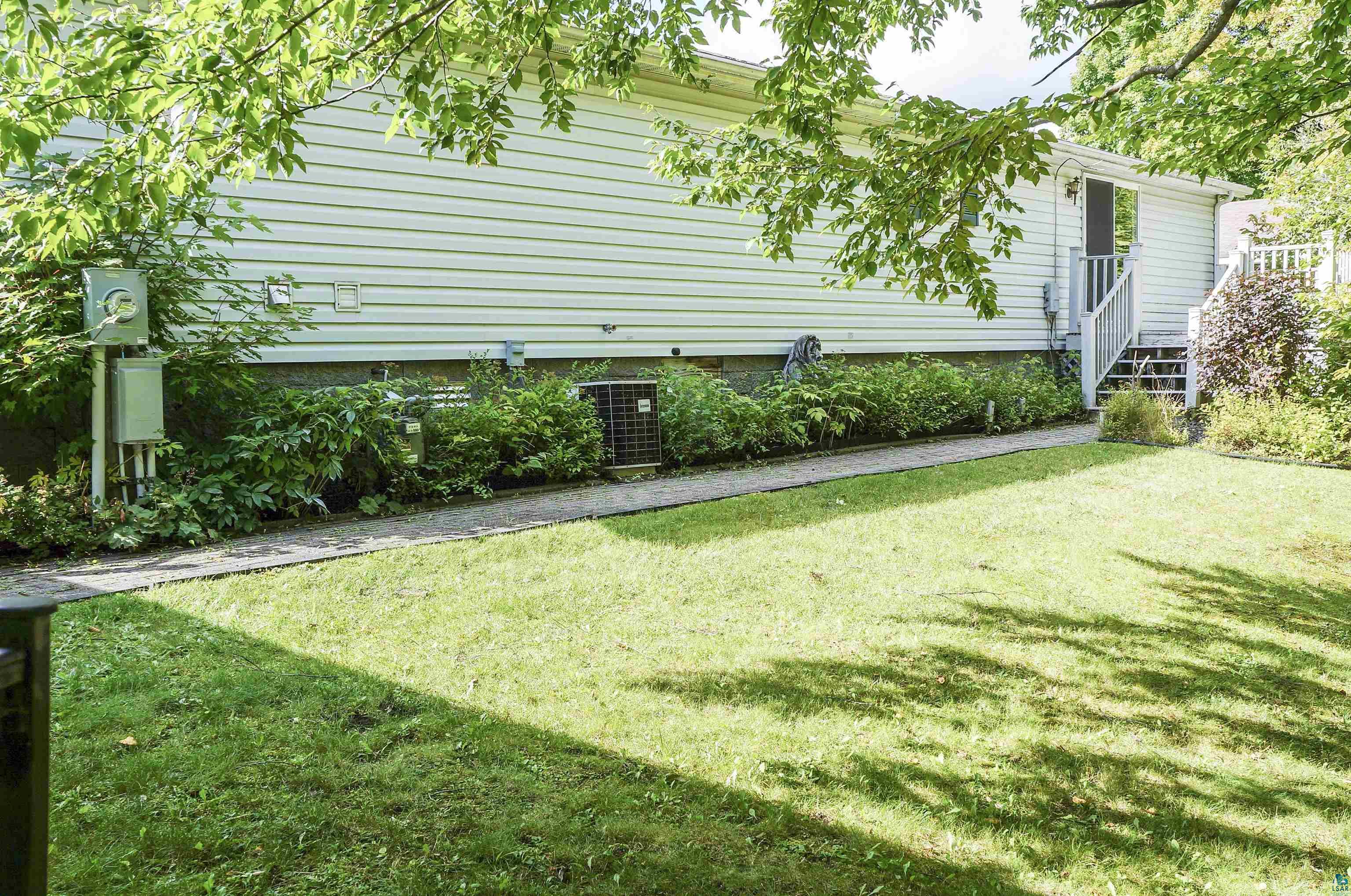 White-sided house with raised entry stairs, shrubs, and a sunny lawn.
