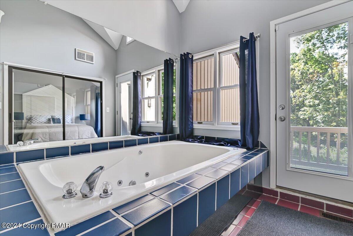 Bathroom with a jetted soaking tub framed by blue tile and a mirrored wall.