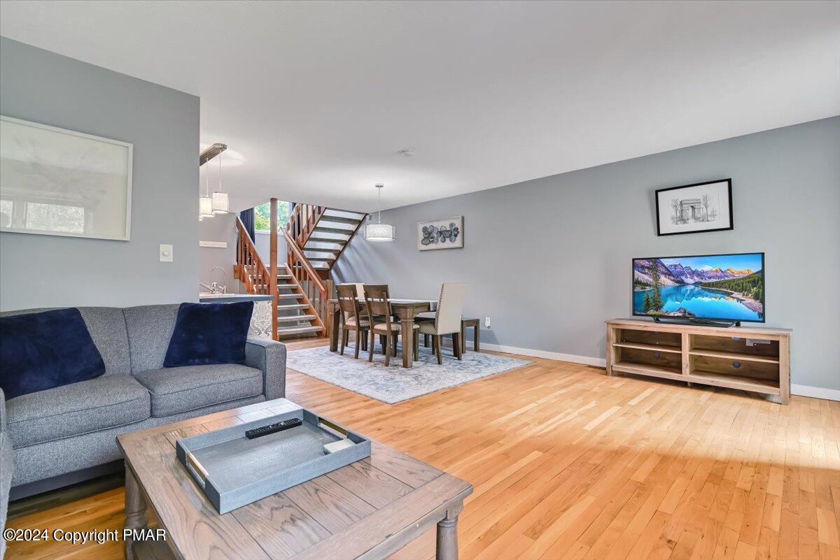 Living and dining room with hardwood floors, gray sofa, dining set, and open staircase.