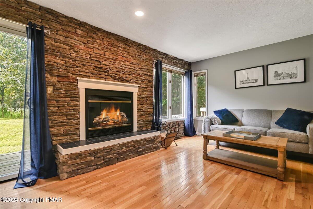 Living room with a stone fireplace, hardwood floors, and a gray sofa beside large windows.