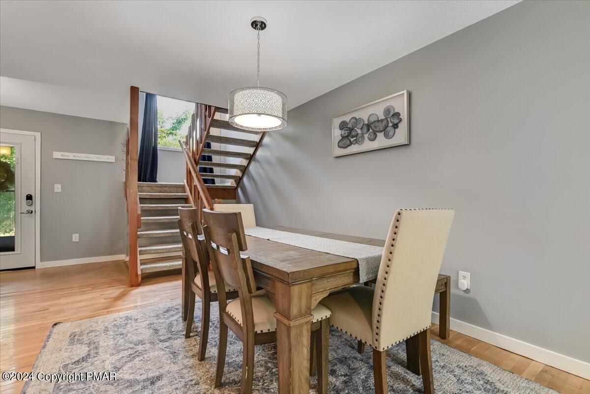Dining room with a wooden table, upholstered chairs, patterned rug, and staircase with wood railings.