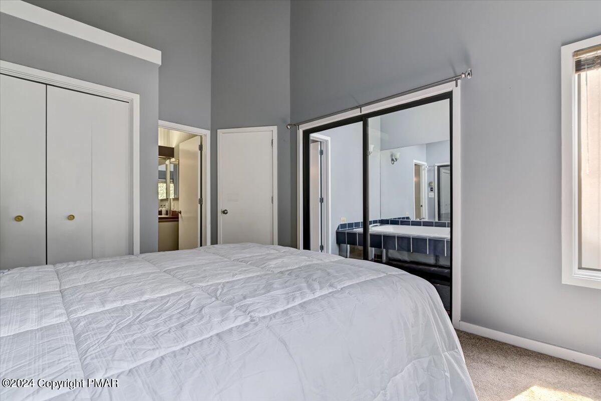 Bedroom with a large white-covered bed, mirrored closet doors, gray walls, and daylight from a window.