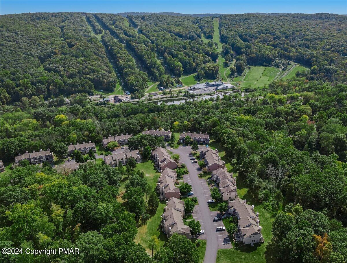 Aerial view of wooded townhouse community with a river and green slopes in the distance.
