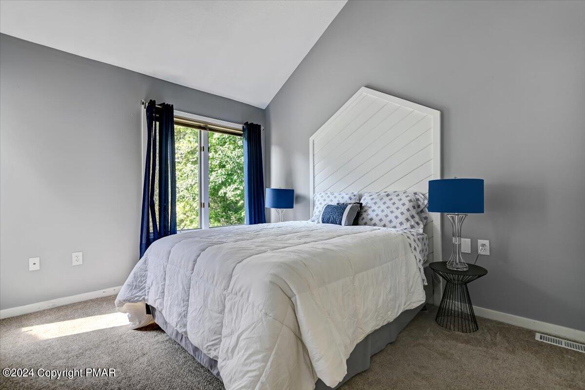 Bedroom with a white bed, tall geometric headboard, blue curtains, and a window overlooking trees.