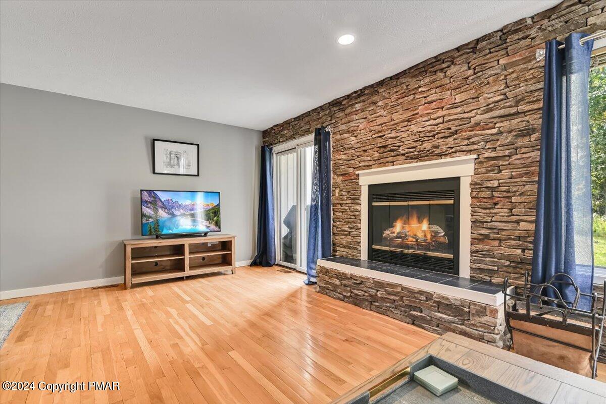 Living room with a tall stone fireplace, hardwood floors, and blue-curtained glass doors.