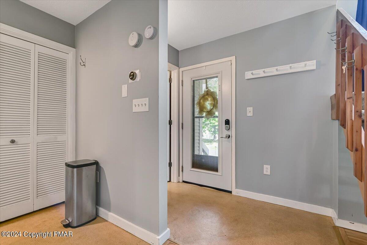Entryway with a glass-panel door and wreath, louvered closet doors, and wall hooks.