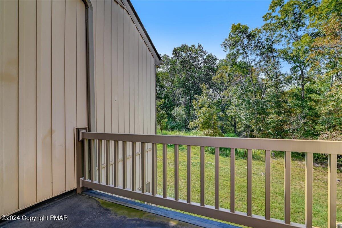 Small deck with brown railing overlooks a grassy yard and trees.
