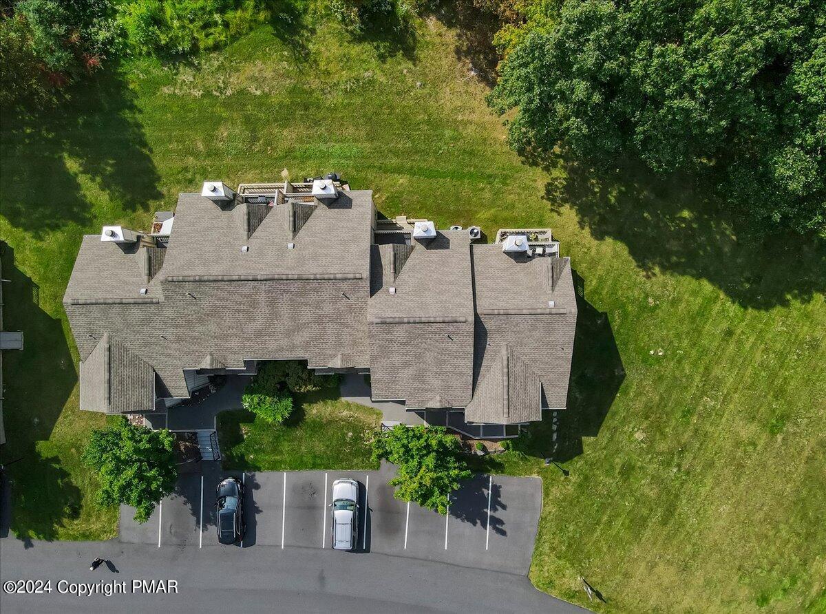 Aerial view of a residential building with a broad gray roof, lawn, trees, and parking area.