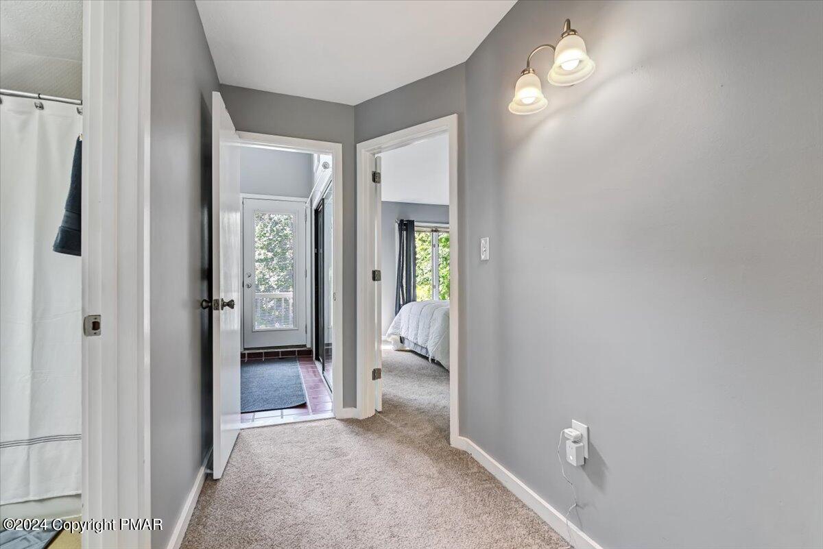 Hallway with gray walls and carpet, leading to a bedroom and glass-paneled door.