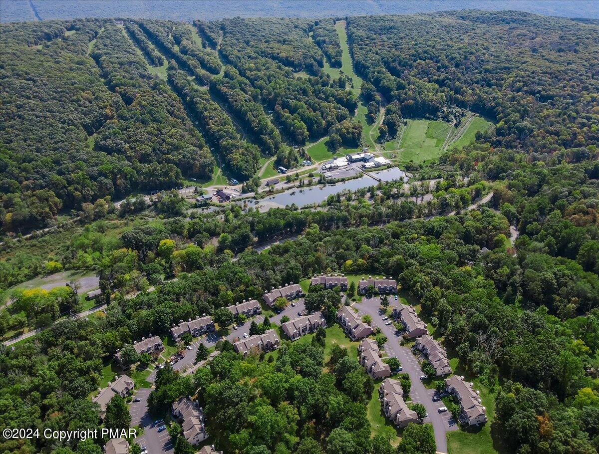 Aerial view of a townhouse community surrounded by woodland, with a lake and open fields beyond.