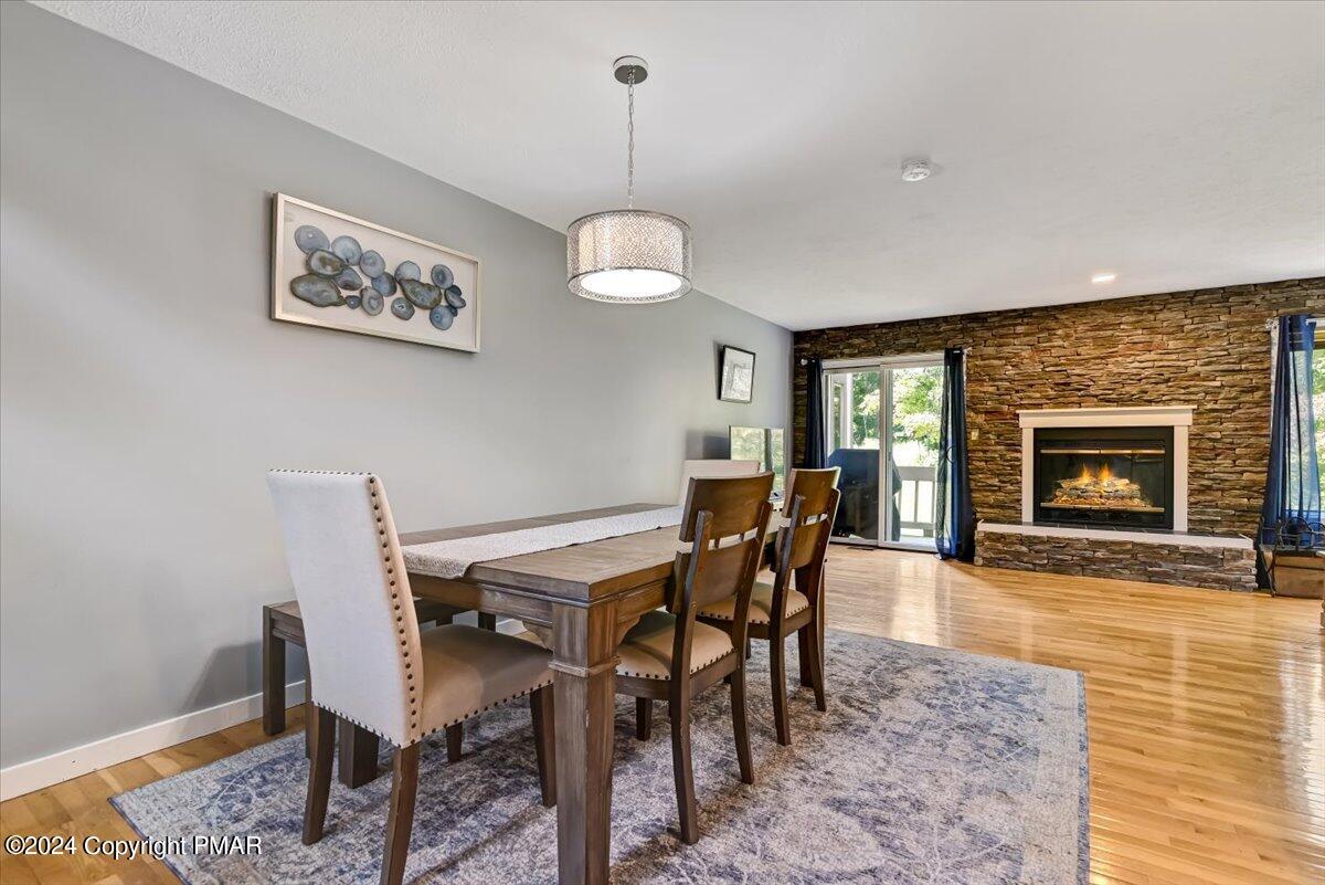 Dining room with a wood table and upholstered chairs beside a stone fireplace.