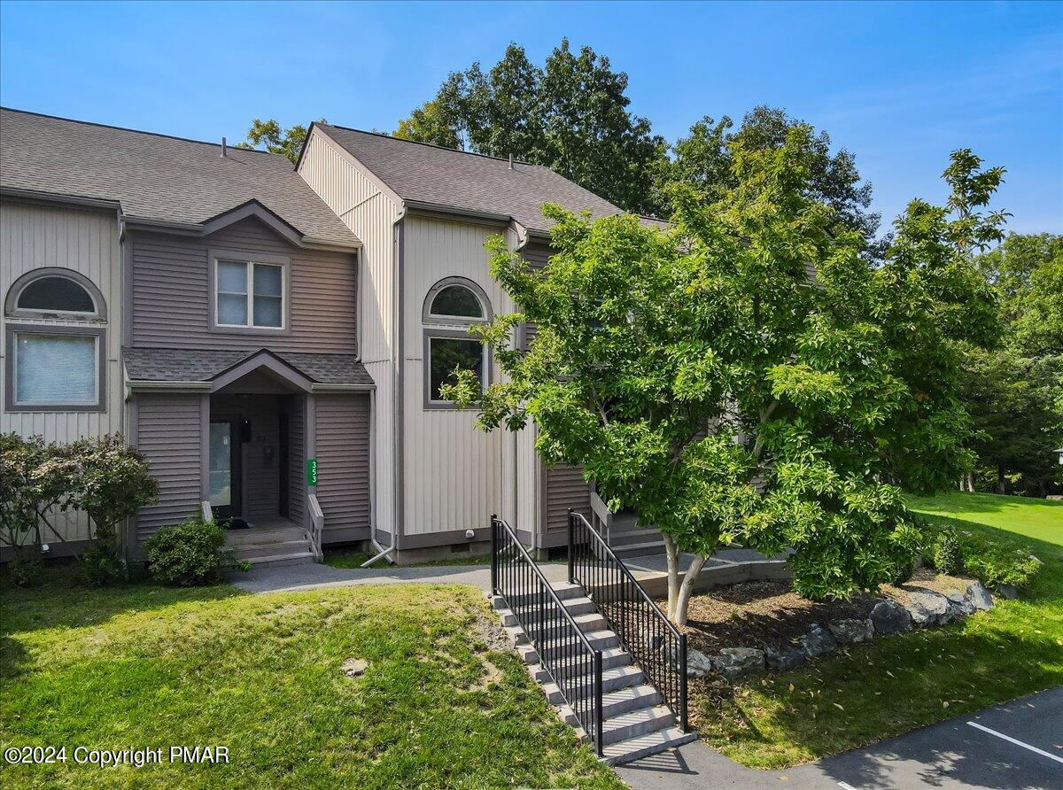 Attached home with gray and cream siding, arched windows, and a landscaped entrance with black-railed steps.