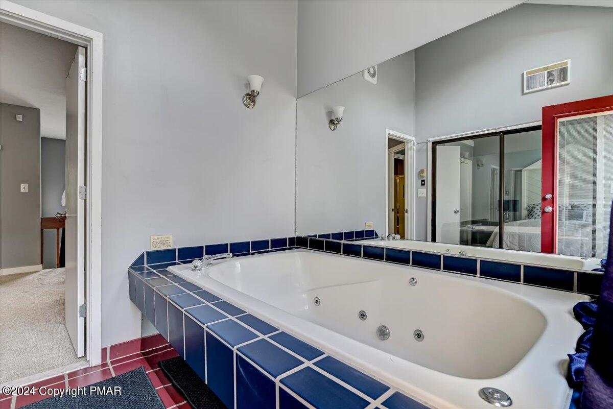 Bathroom with a large jetted tub, dark blue tile surround, and wall-length mirror.