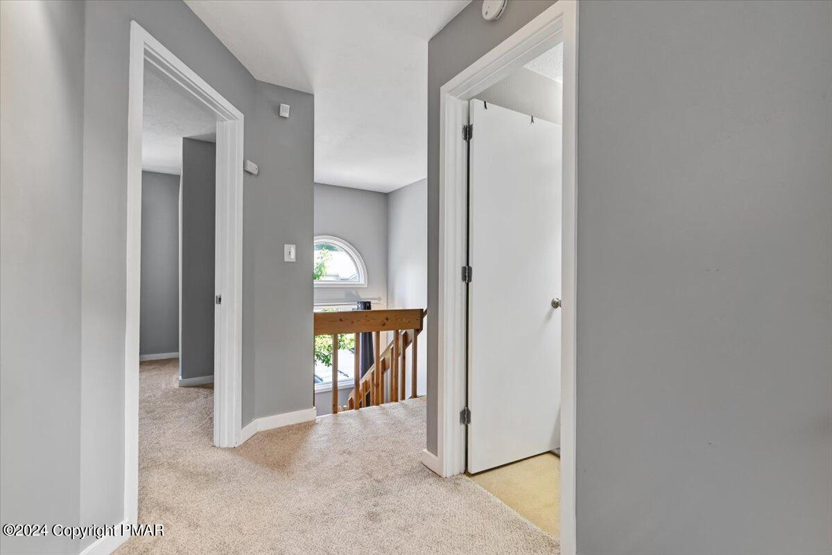 Carpeted upstairs landing with gray walls, open doorways, and a wooden stair railing.