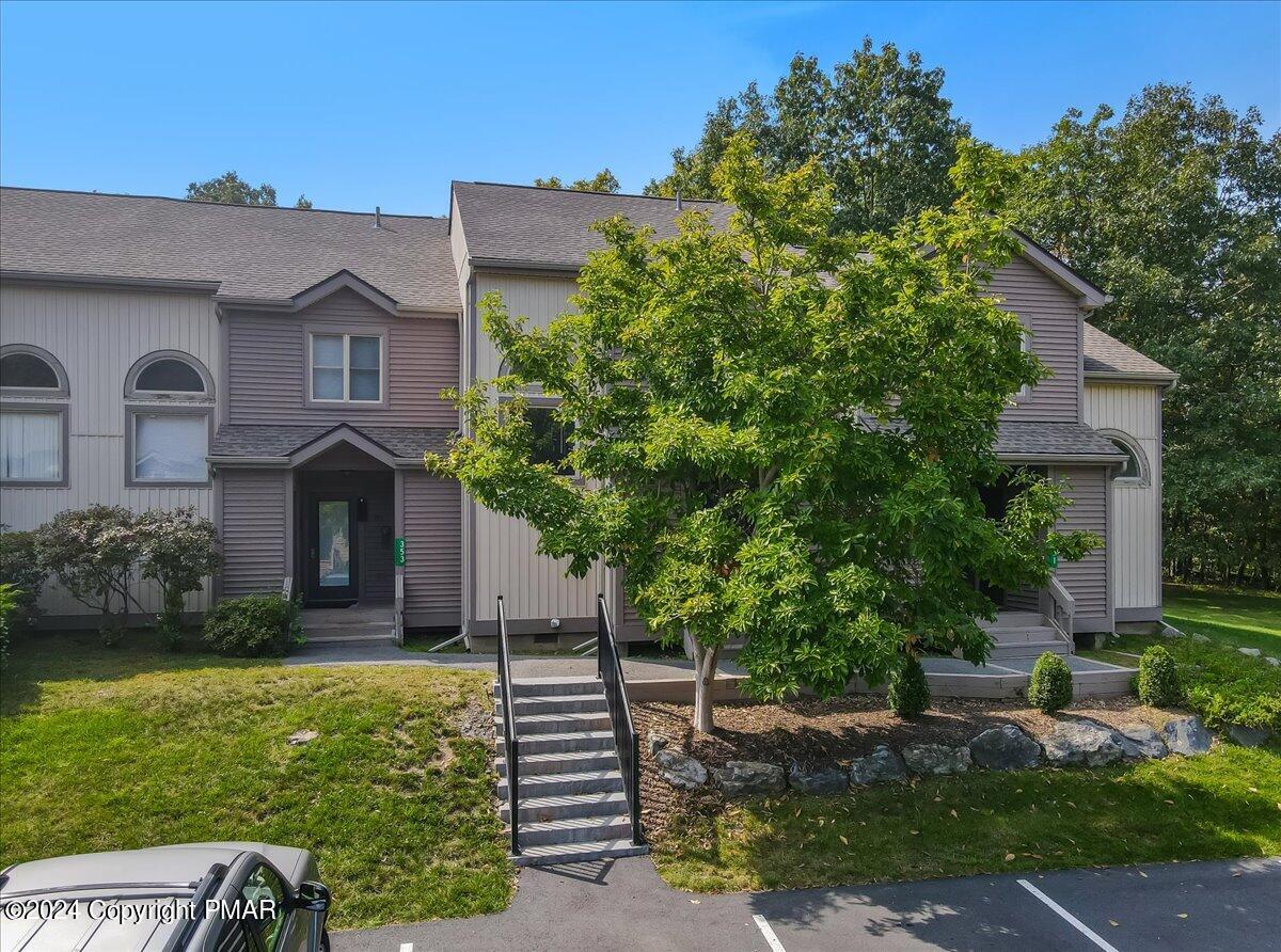 Gray multi-level residence with front steps, landscaped lawn, and a large tree partly obscuring the facade.