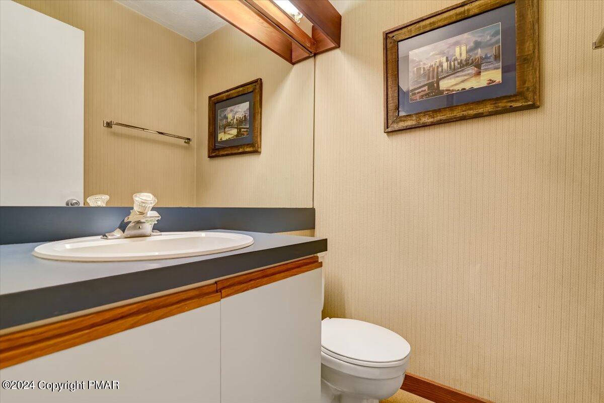 Bathroom vanity with an oval sink, dark countertop, wood trim, and toilet beneath framed artwork.
