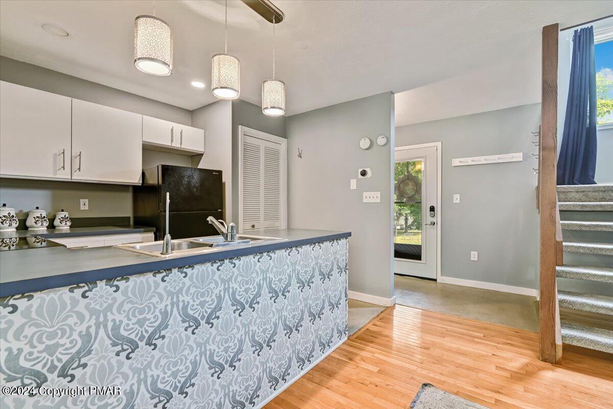 Kitchen with a patterned peninsula, white cabinets, black refrigerator, and hardwood flooring beside the entry stairs.