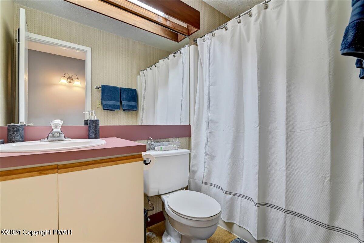 Bathroom with pink countertop, cream vanity, toilet, and white shower curtain.
