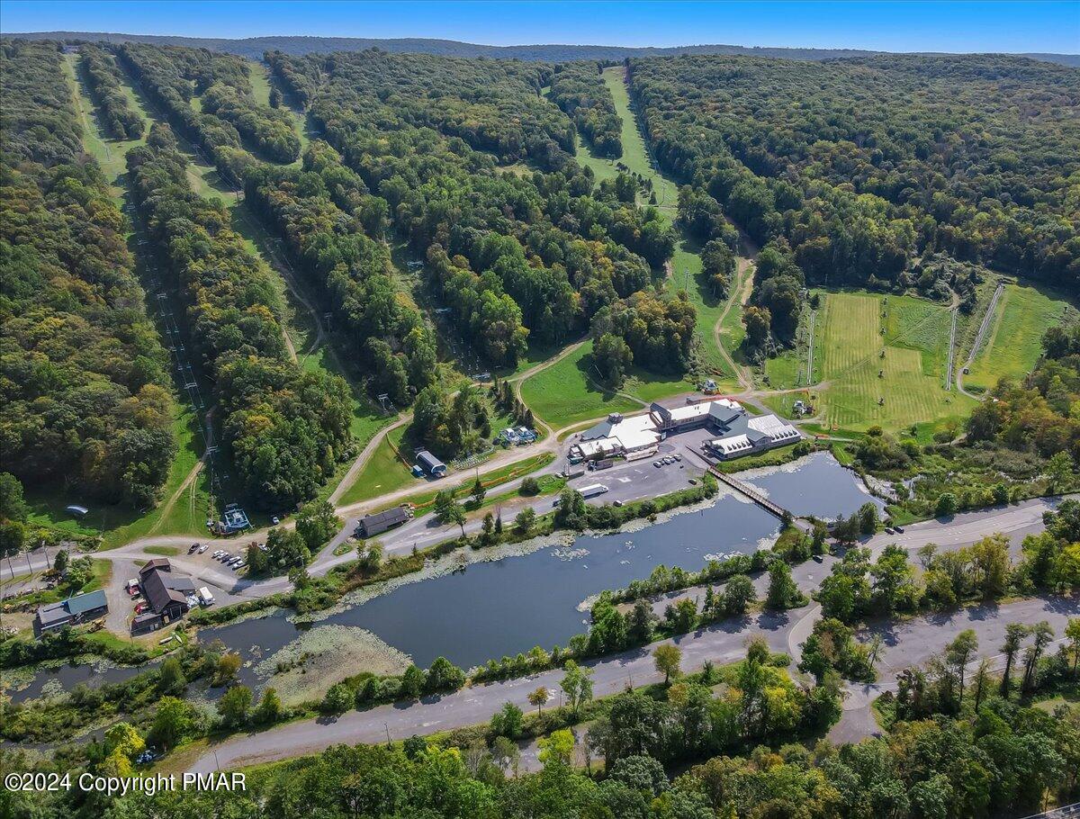 Aerial view of a large property complex beside a pond, surrounded by wooded hills and open grounds.
