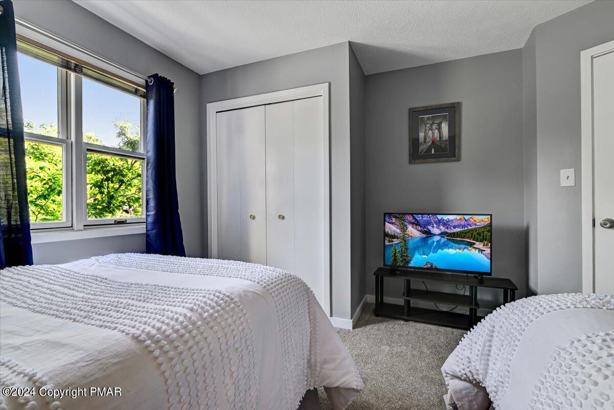 Bedroom with two white-covered beds, navy curtains, a double-door closet, and a television.