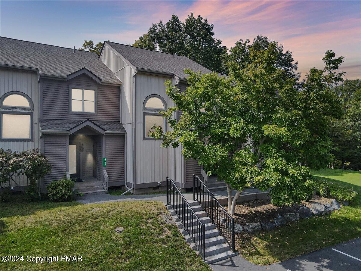 Gray townhouse exterior with arched windows, leafy trees, and black-railed front steps at dusk.