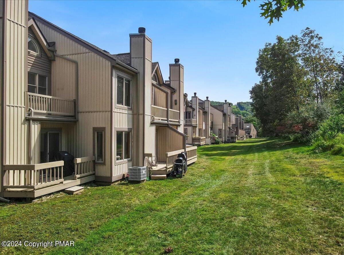 Attached beige townhomes with balconies line a broad grassy lawn beneath a clear blue sky.