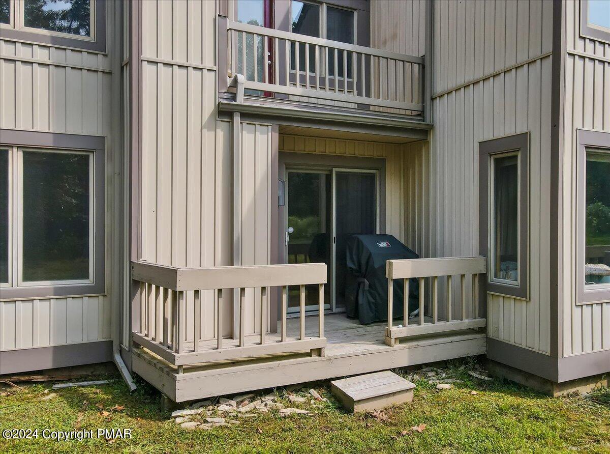 Home exterior with a small deck, sliding glass door, covered grill, and balcony above.