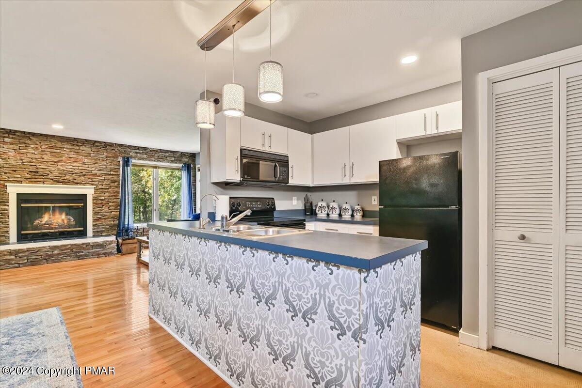Open-plan kitchen with a patterned island and white cabinets beside a stone fireplace.