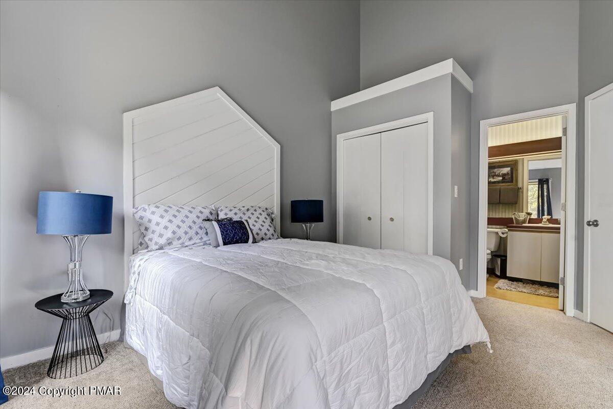 Staged bedroom with a white bed, angular paneled headboard, blue lamps, and bathroom visible through the doorway.