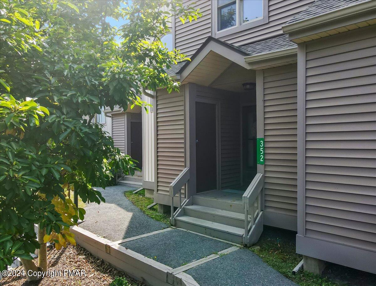 Townhome entrance with covered porch, gray siding, front steps, and landscaped walkway.