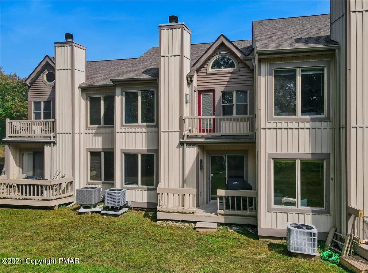Multi-level townhouse exterior with balconies, a red entry door, and a grassy yard.