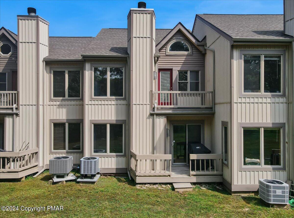 Attached residence rear exterior with beige siding, balconies, central entrance, and ground-level air-conditioning units.