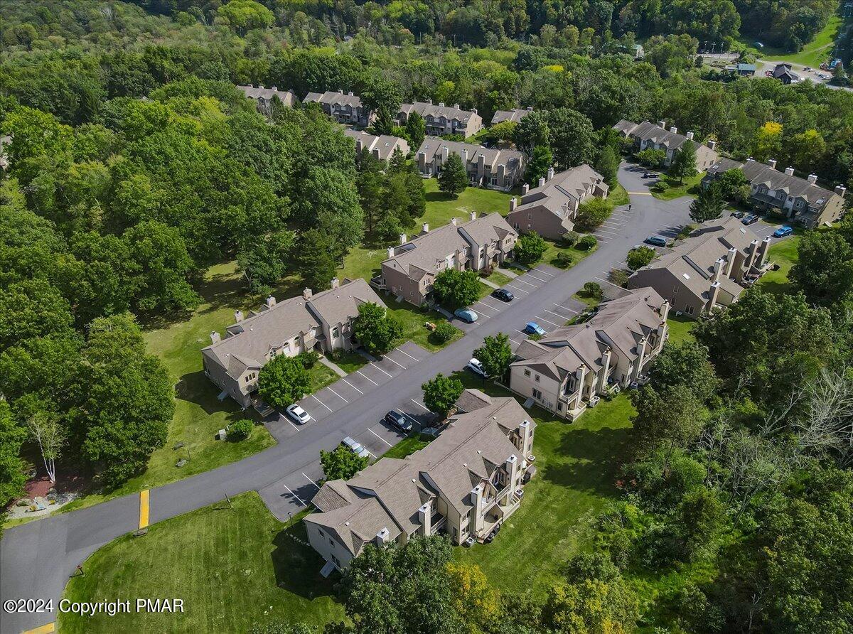 Aerial view of attached townhomes, parking areas, and lawns surrounded by mature trees.