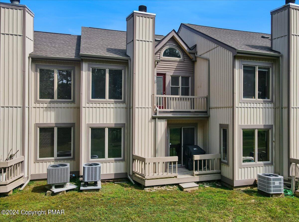 Rear exterior of a beige-sided residence with multiple chimneys, a small balcony, and outdoor air-conditioning units.