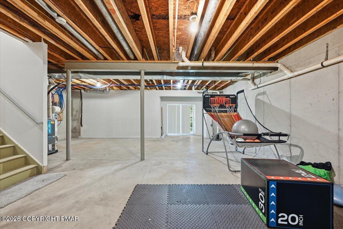 Unfinished basement recreation area with exposed joists, a basketball arcade game, and exercise equipment.