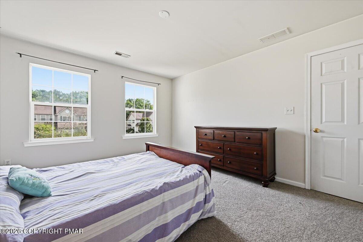 Bedroom with a striped lavender-and-white bedspread, dark wood dresser, and two windows.
