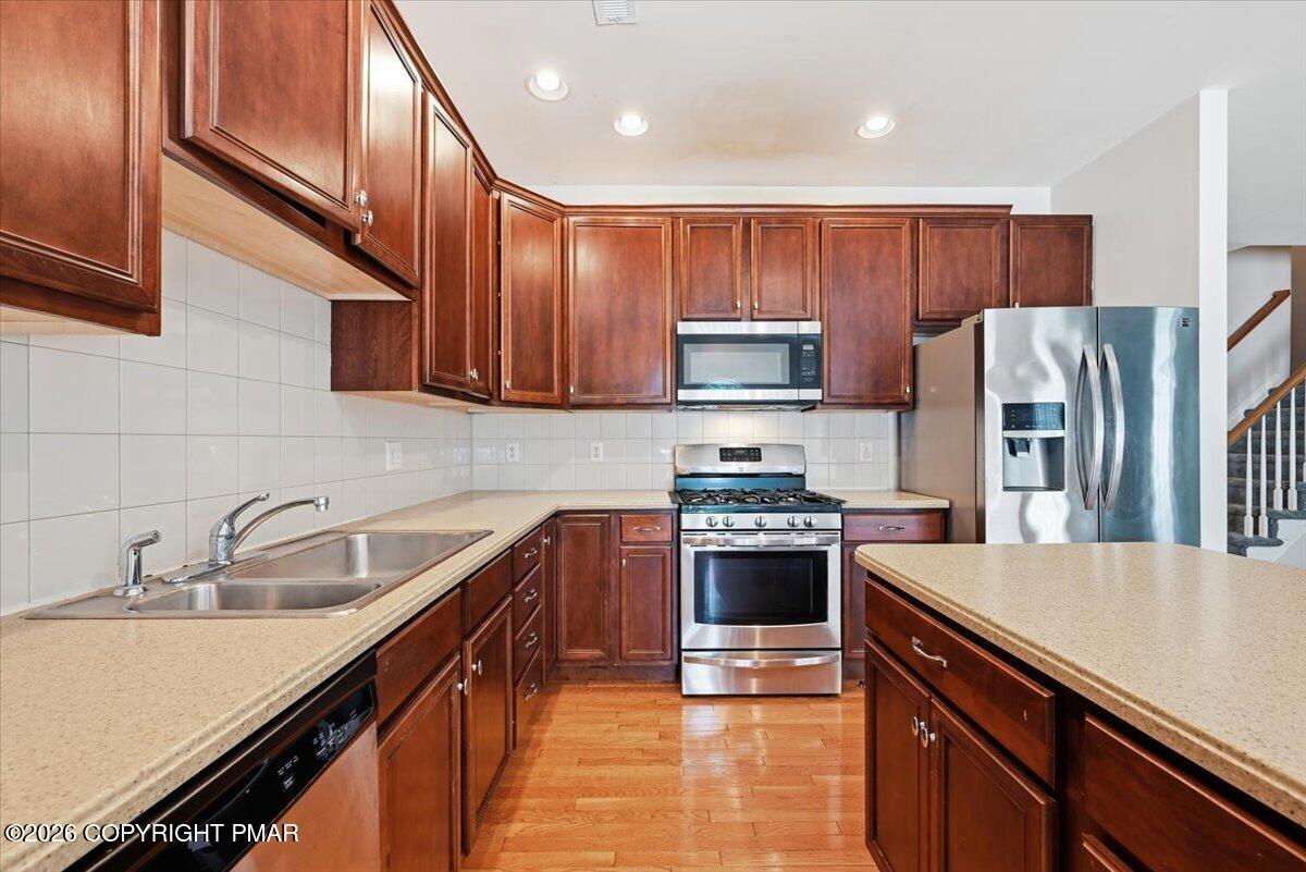 Kitchen with dark wood cabinets, stainless steel appliances, double sink, and wood flooring.