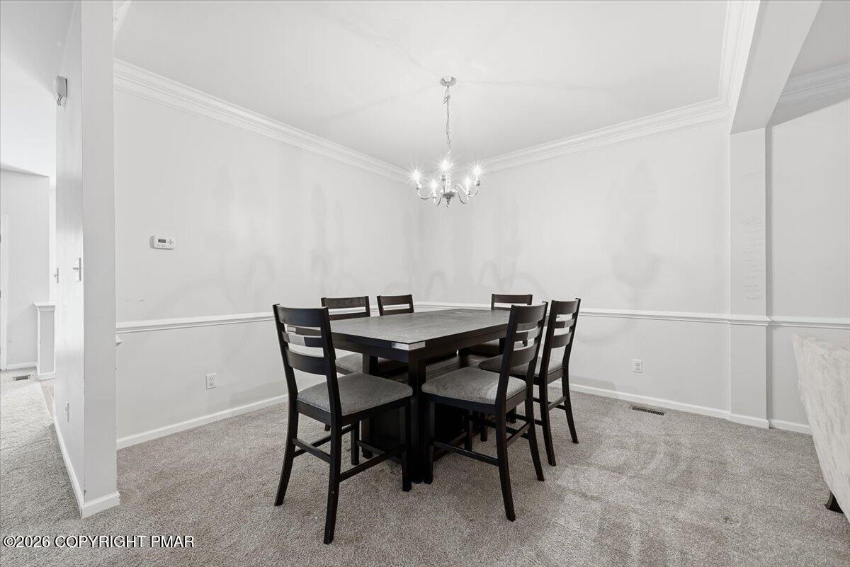 Dining room with a dark table, six chairs, gray carpet, and a chandelier.