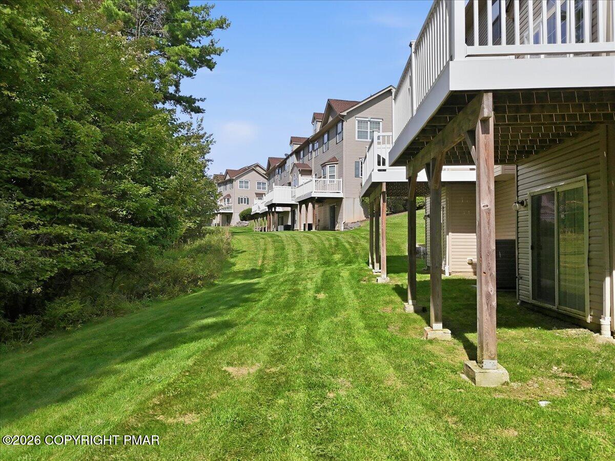 Attached homes with elevated rear decks above a sloping lawn bordered by trees.