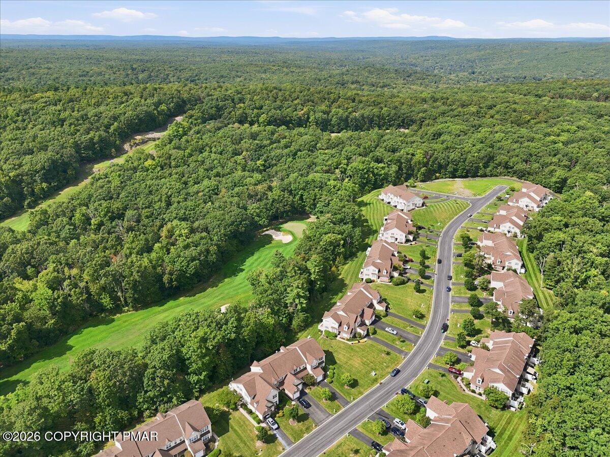 Aerial view of homes along a curving road beside a golf course fairway and wooded hills.