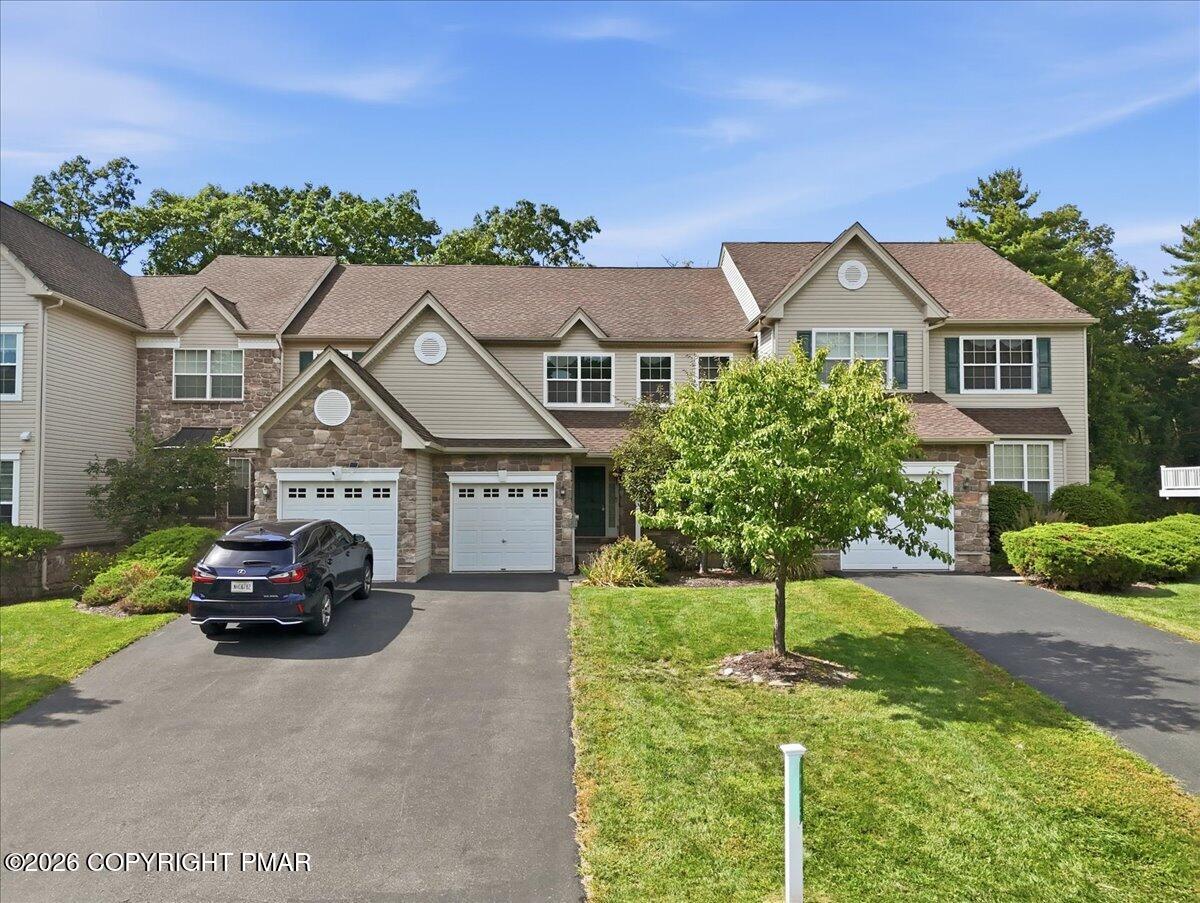 Large two-story home with stone accents, multiple garage doors, and a tree-lined front lawn.