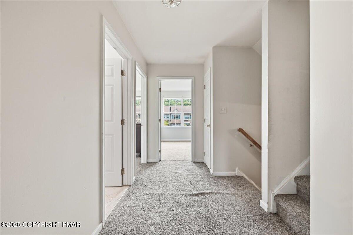 Carpeted hallway with several doorways and stairs beside a window at the far end.