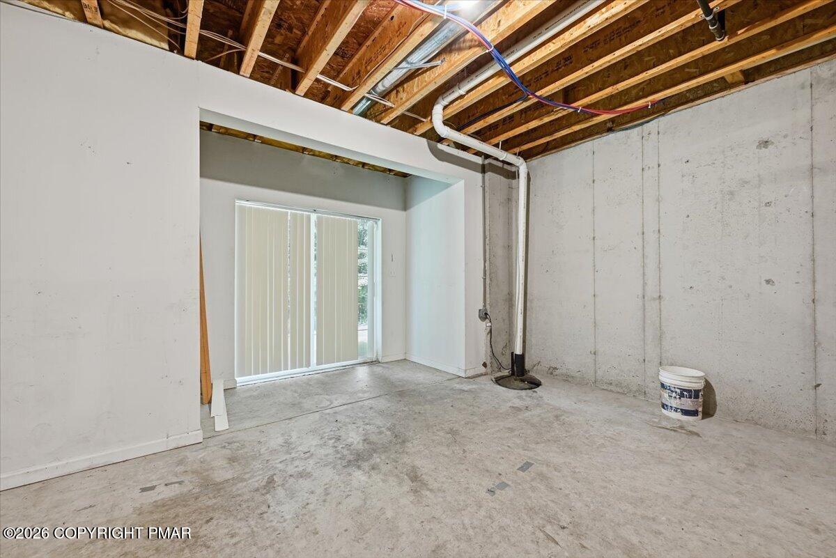 Unfinished basement with exposed joists, concrete walls, and a sliding glass door with vertical blinds.