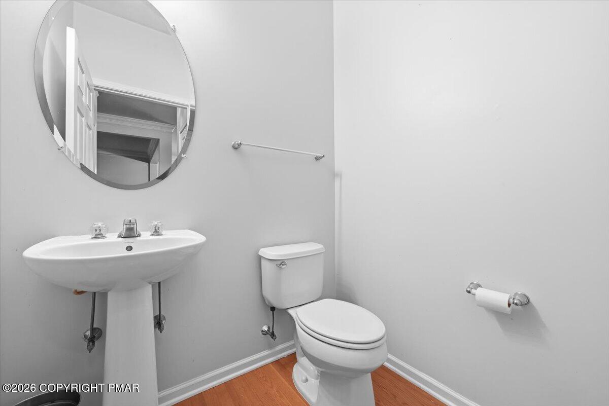 Bathroom with a pedestal sink, toilet, large round mirror, and warm-toned wood flooring.
