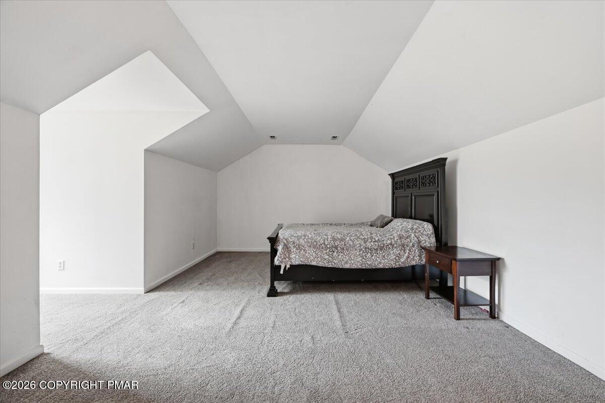 Bedroom with vaulted ceiling, carpeted floor, and dark wood bed with patterned bedding.