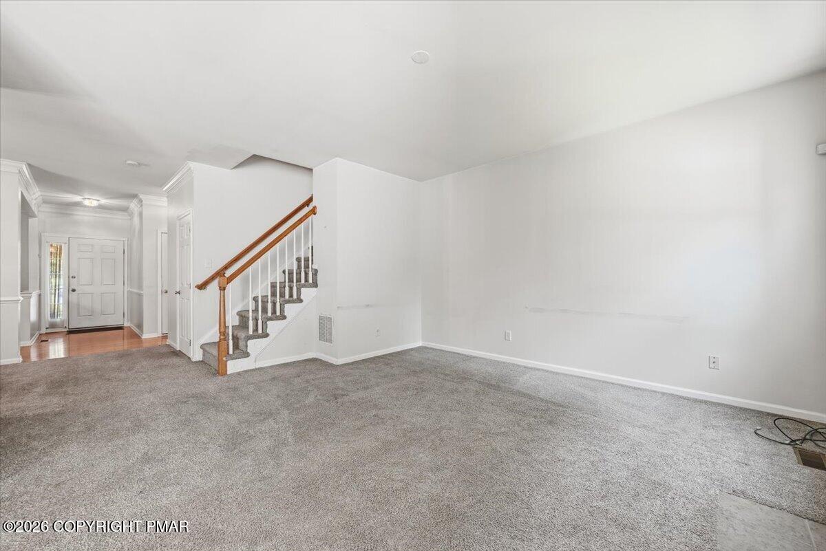 Unfurnished living room with gray carpeting and a staircase beside the front entry.