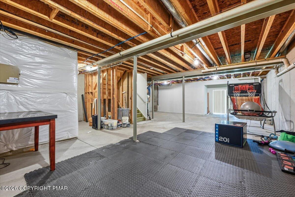 Basement with exposed ceiling joists, exercise mats, and a basketball hoop.