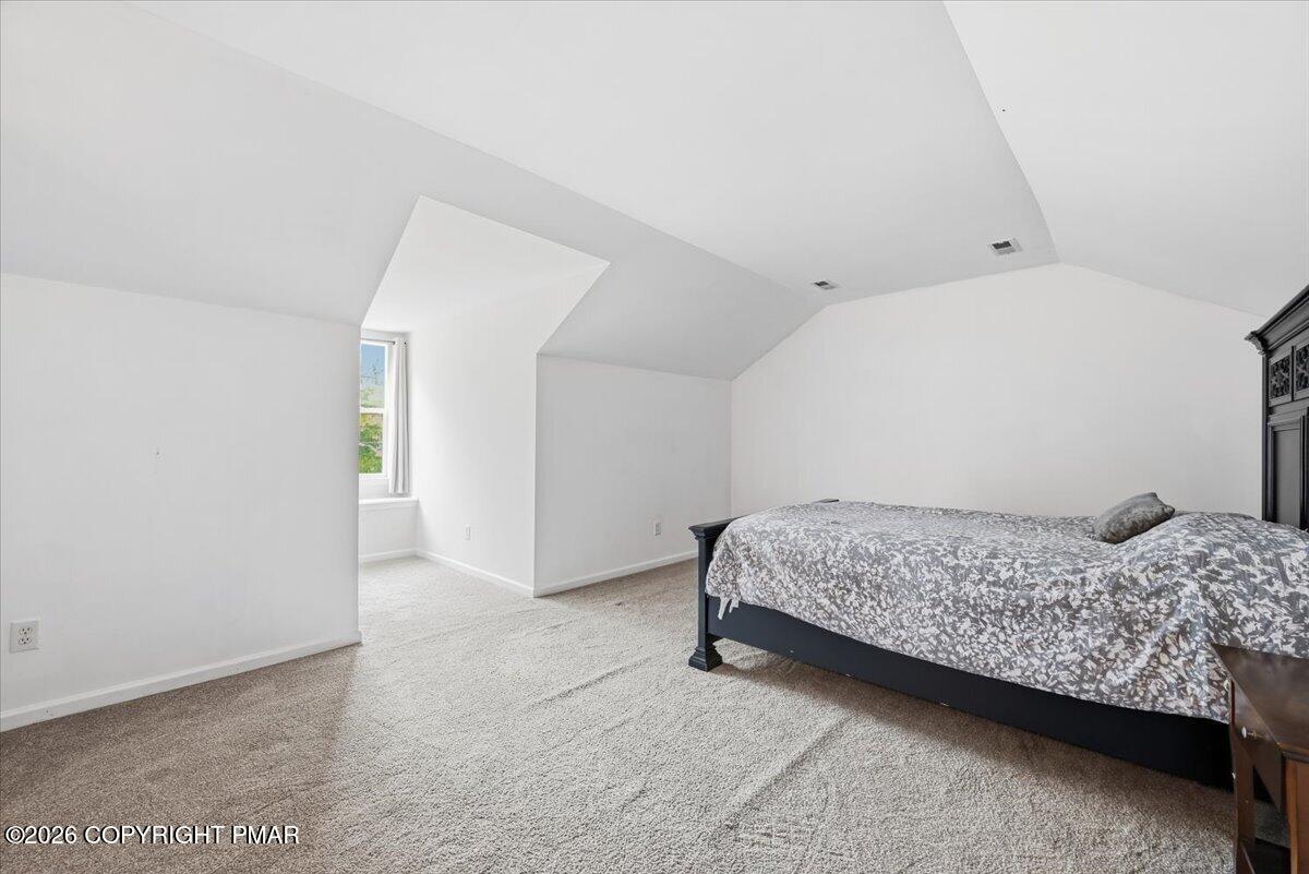 Spacious bedroom with a large bed, gray patterned bedding, carpet, and an angled ceiling.