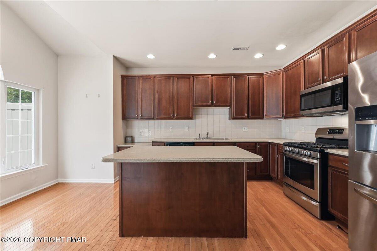 Kitchen with a large island, dark wood cabinetry, stainless steel appliances, and hardwood floors.