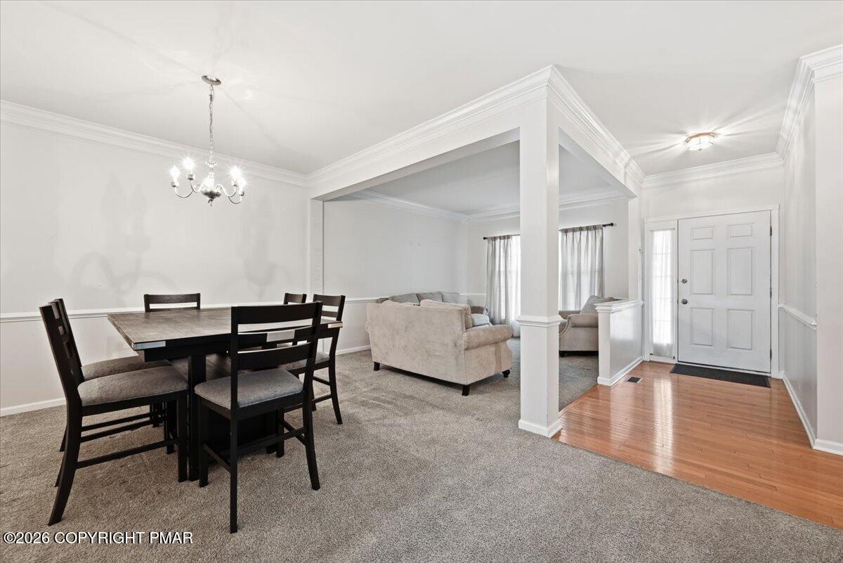 Open dining and living area with dark dining set, carpeted seating space, and hardwood entry.